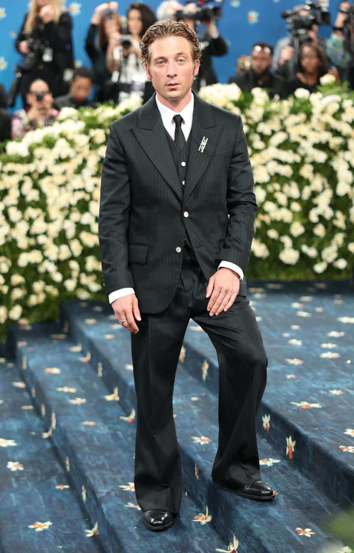 Jeremy Allen White viste un Louis Vuitton by Men's, del director creativo Pharrell Williams. El traje de tres piezas, hecho a medida, consta de una chaqueta con chaleco y pantalones acampanados, tejidos en fino jacquard de lana de raya diplomática. Lo combinó con una camisa de algodón blanco y una corbata de seda negra. El actor lució, además, un broche en la solapa.